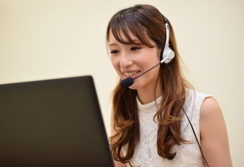 Woman wearing a headset with microphone, smiling at a laptop screen.
