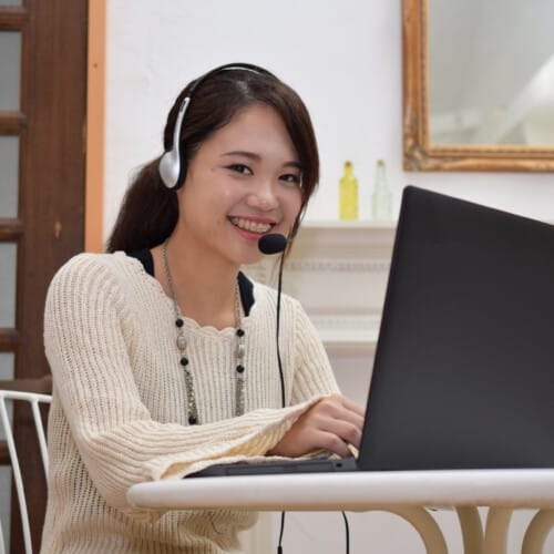 Smiling young woman wearing a headset sits at a table with a laptop.