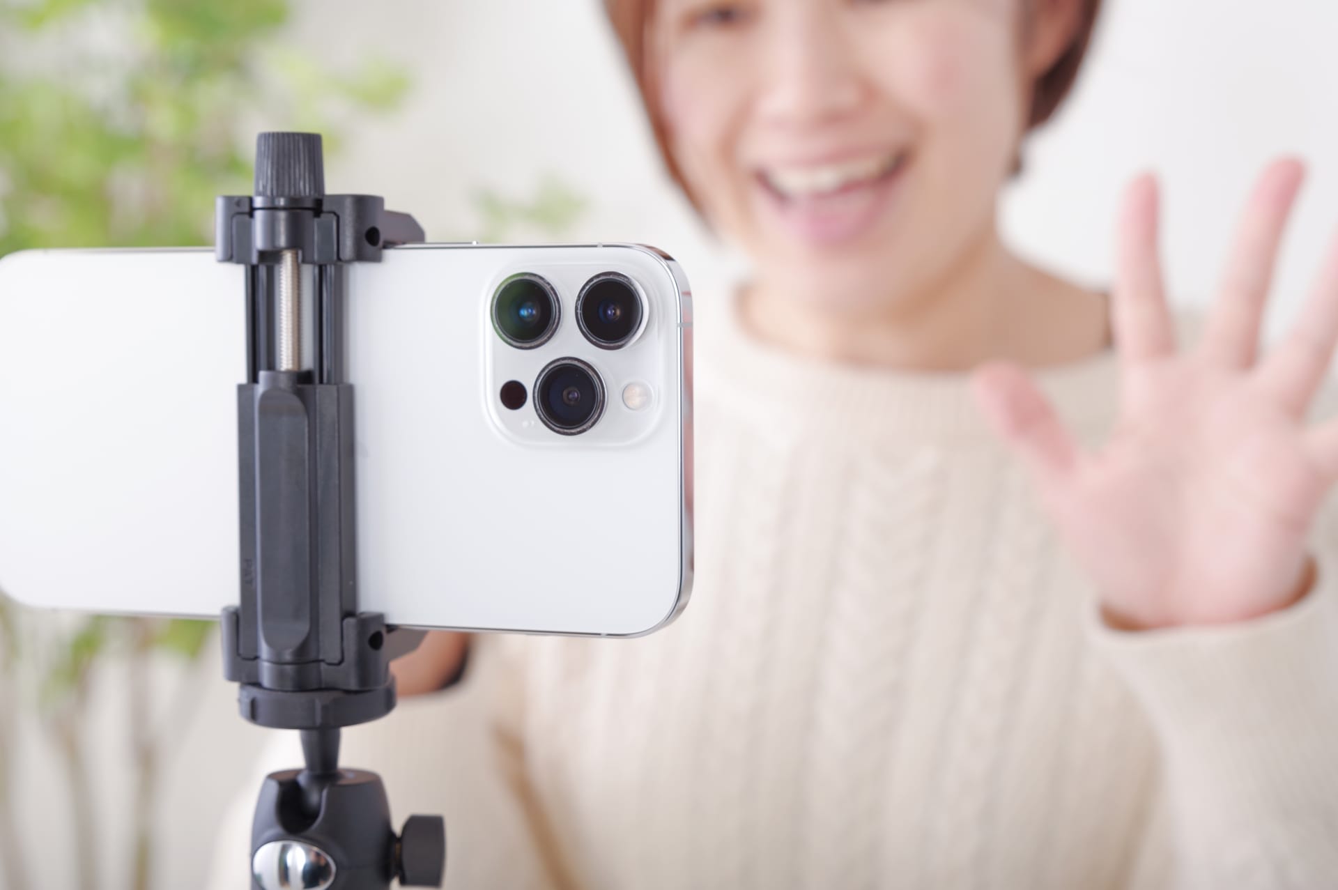 Person taking a selfie with a smartphone mounted on a tripod, waving hello toward the camera.