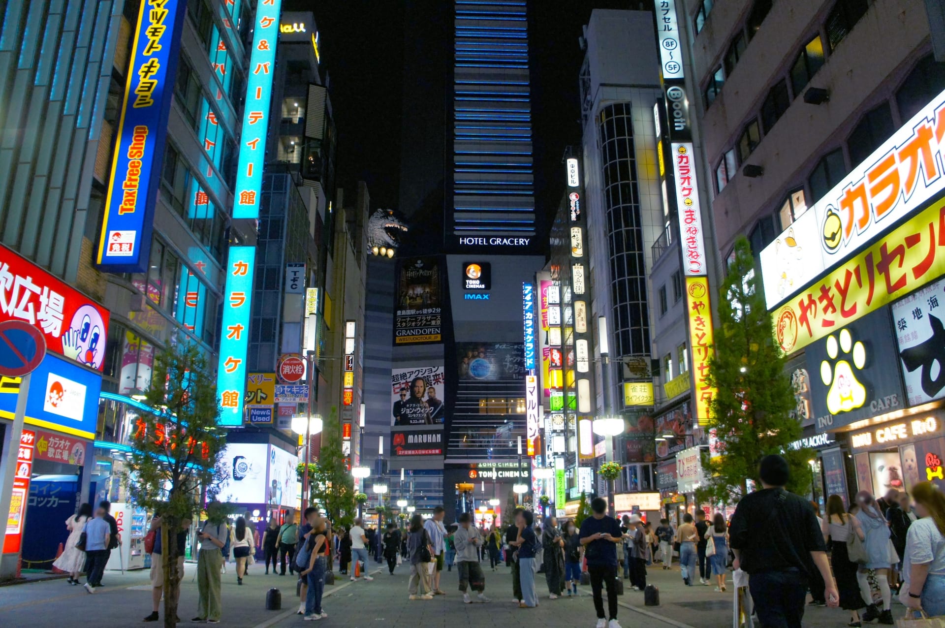 Busy neon-lit street in Japan at night with pedestrians and tall colorful signs along both sides of the avenue.