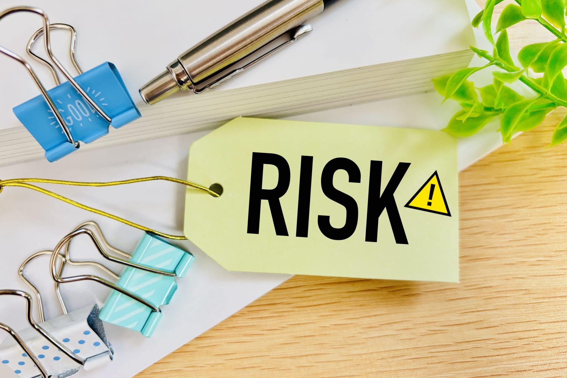 Yellow tag with the word RISK and a warning triangle on a desk among office supplies like clips and a pen