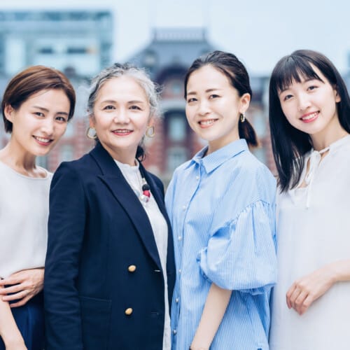 Four women posing together outdoors on a city street, smiling at the camera.