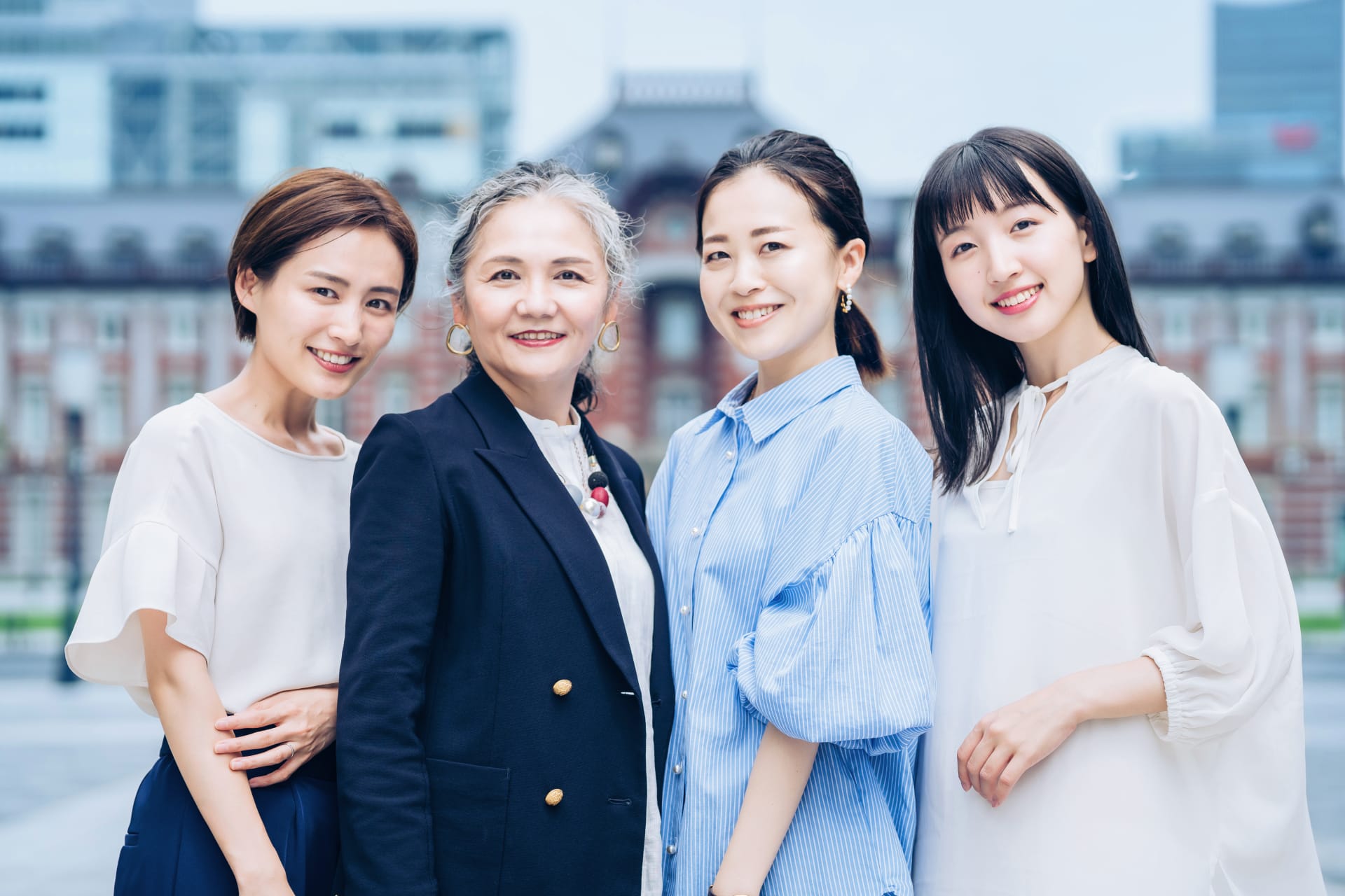 Four women posing together outdoors on a city street, smiling at the camera.