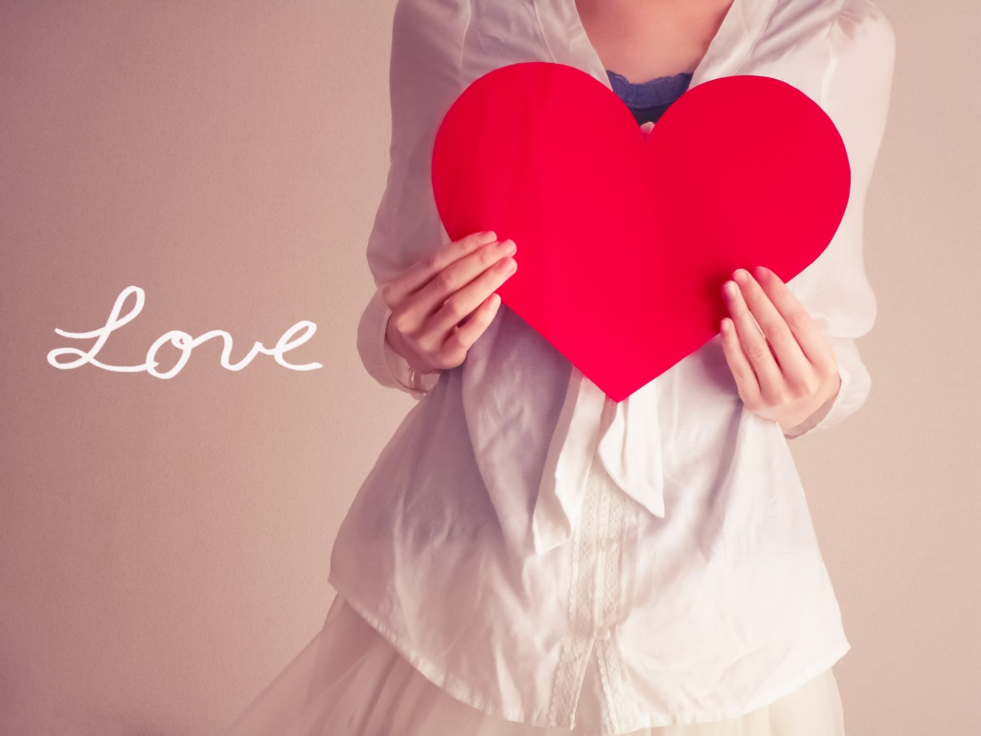 1620991_m - Belle Work Person in a white outfit holds a large red heart, with the word 'Love' written in white on the left side.