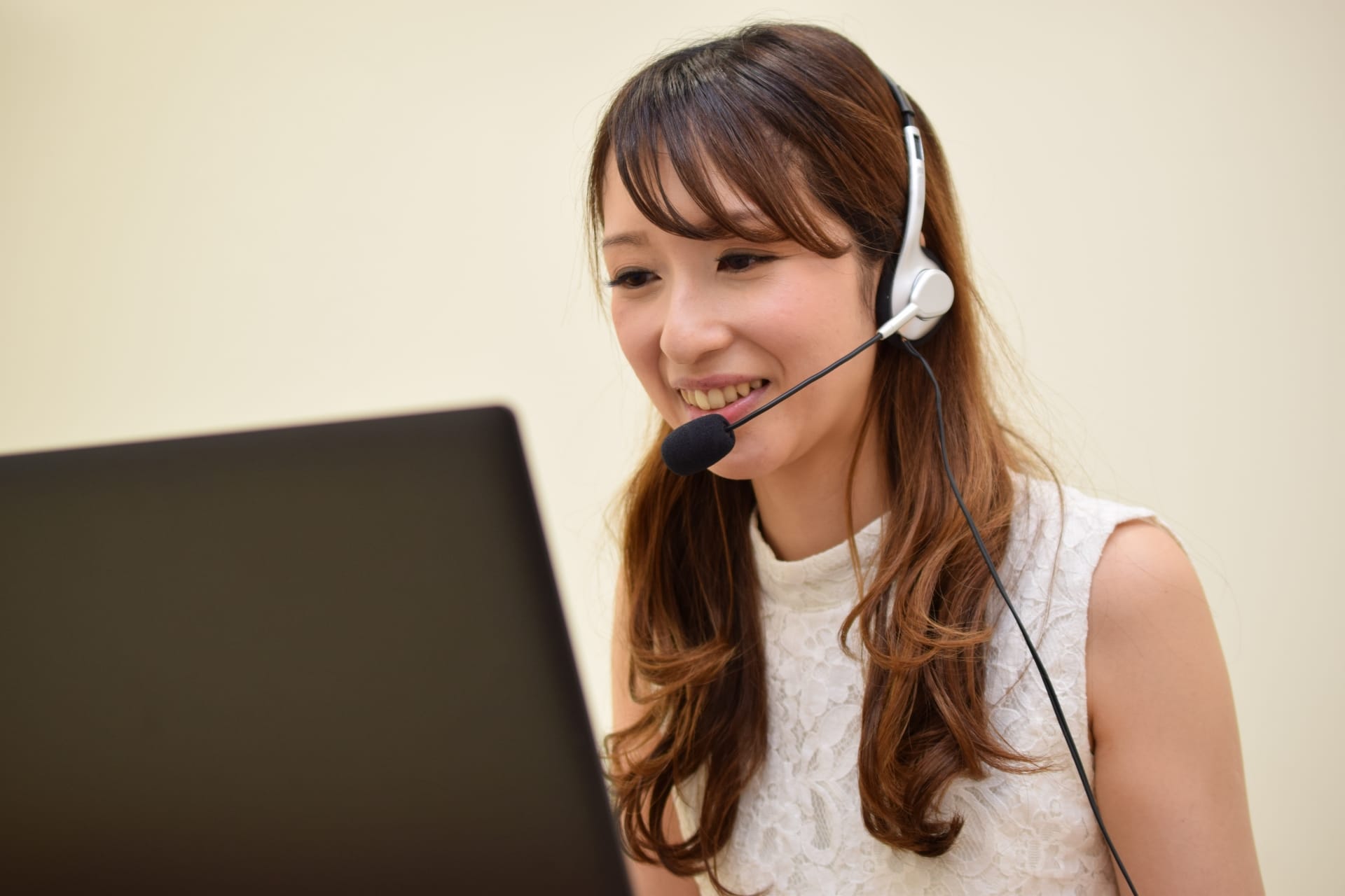 1807570_m - Belle Work Smiling woman wearing a headset with microphone while looking at a laptop, likely a call center or customer service agent.