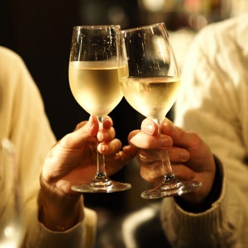 Three people in sweaters clinking stemmed wine glasses for a toast, hands visible.