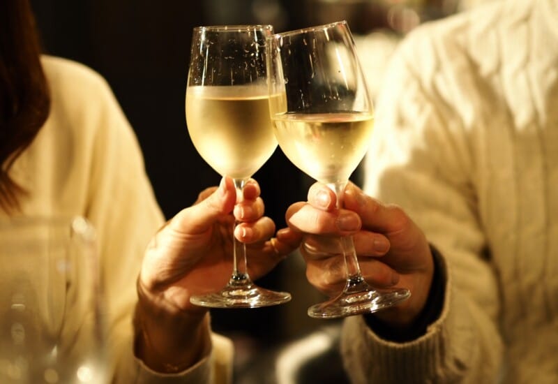 Three people in sweaters clinking stemmed wine glasses for a toast, hands visible.