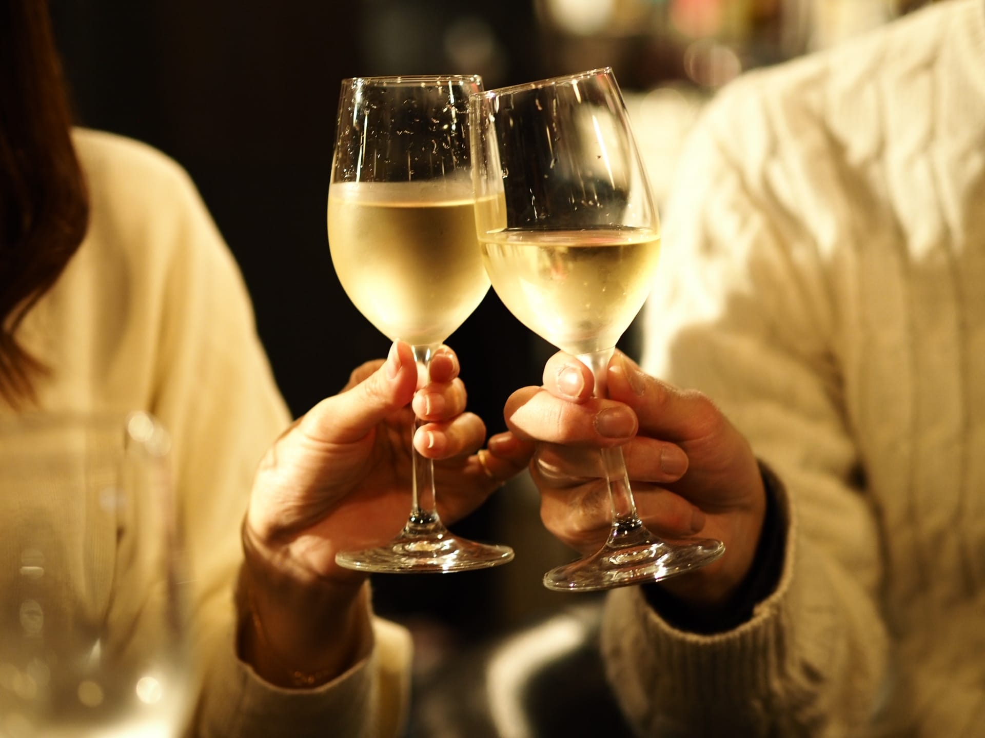 Three people in sweaters clinking stemmed wine glasses for a toast, hands visible.
