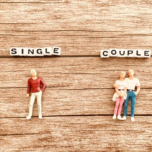 On a wood background, bead-letter signs spell 'SINGLE' on the left and 'COUPLE' on the right, with figures representing a lone person and a small family respectively.