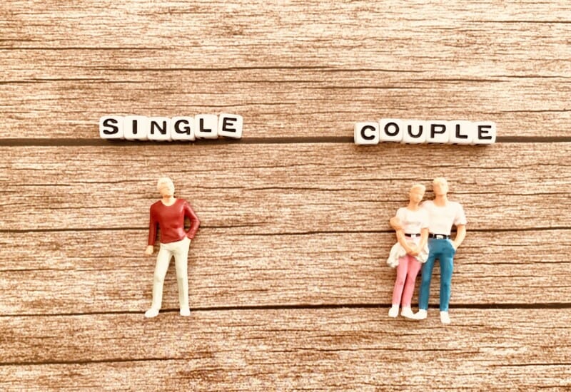 On a wood background, bead-letter signs spell 'SINGLE' on the left and 'COUPLE' on the right, with figures representing a lone person and a small family respectively.