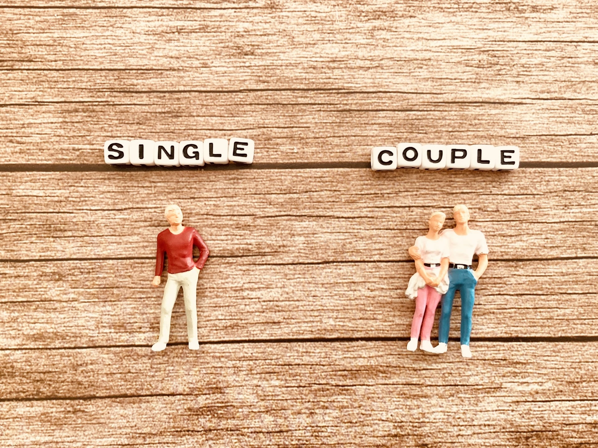 On a wood background, bead-letter signs spell 'SINGLE' on the left and 'COUPLE' on the right, with figures representing a lone person and a small family respectively.