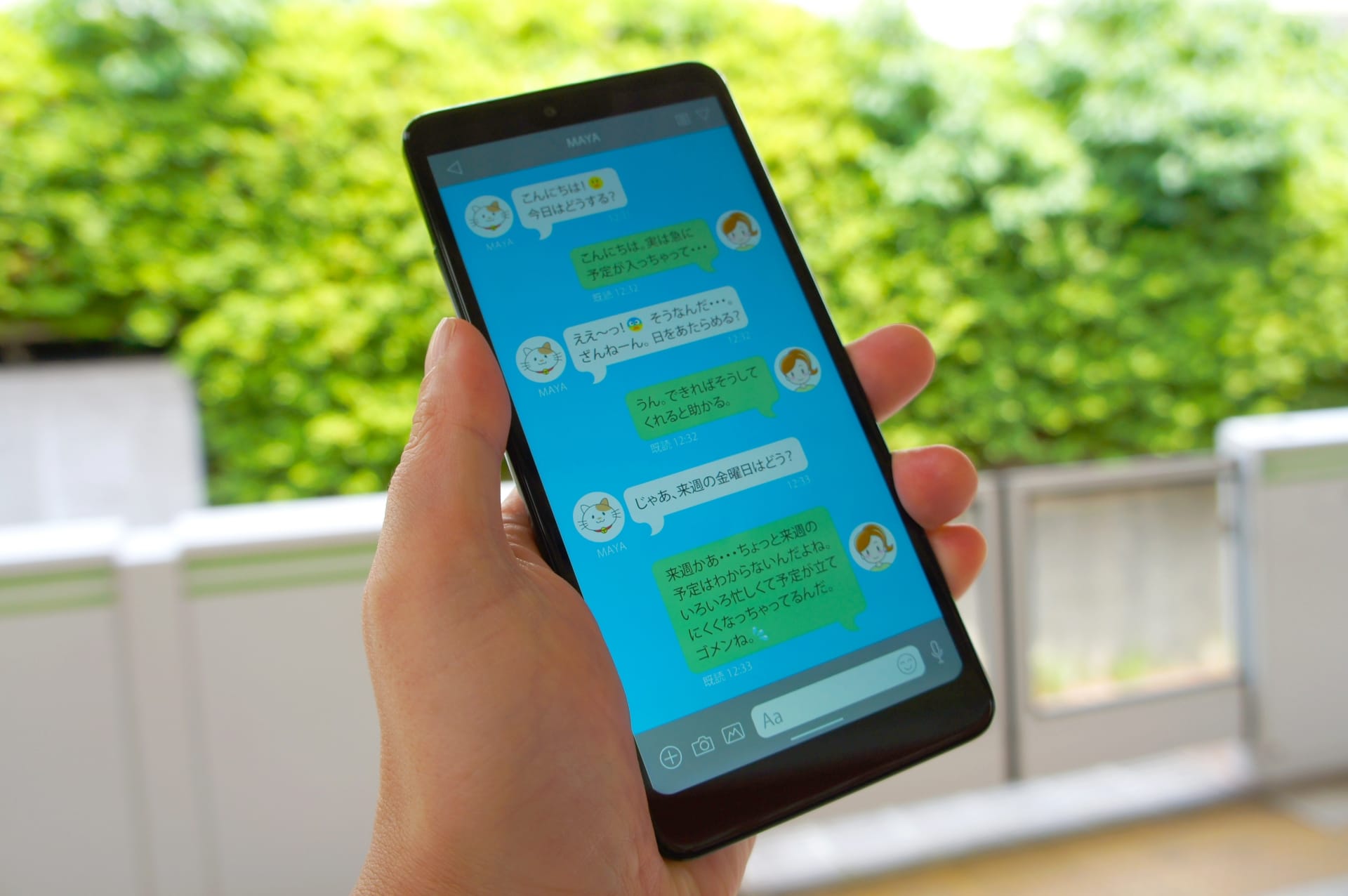 Person holding a smartphone outdoors, screen shows a blue chat app with chat bubbles and avatars (Japanese text).