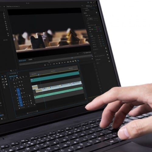 Person edits video on a laptop, with multiple timelines and editing panels visible on screen, hand on keyboard