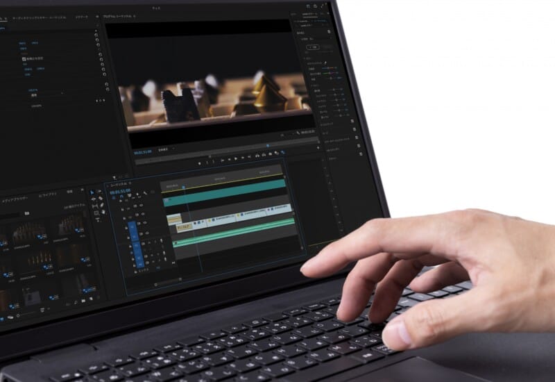 Person edits video on a laptop, with multiple timelines and editing panels visible on screen, hand on keyboard