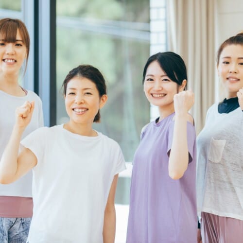 Four smiling women standing side by side indoors, each with a clenched fist raised in celebration.