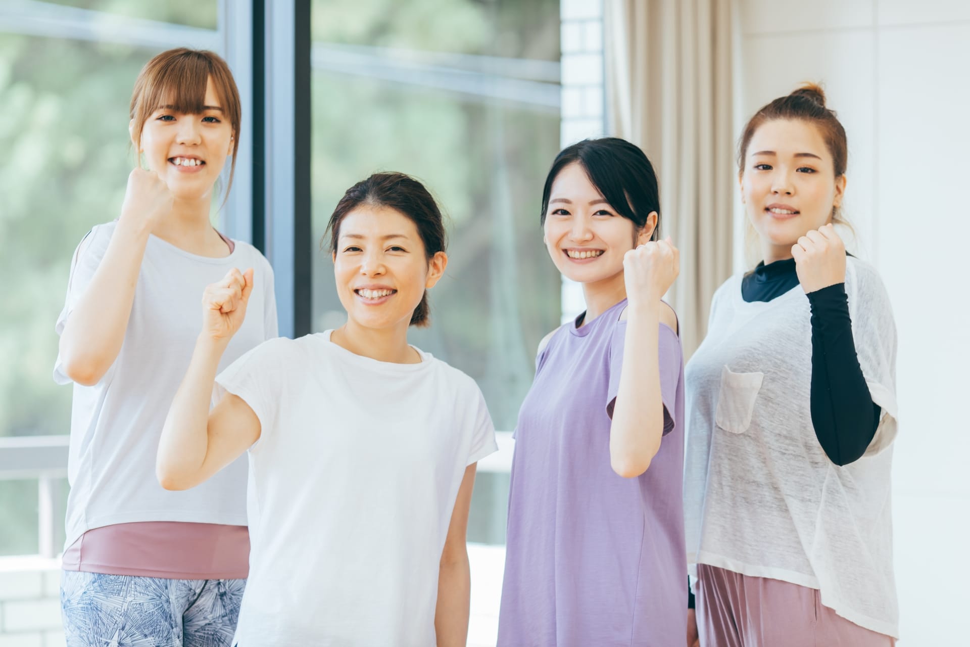 Four smiling women standing side by side indoors, each with a clenched fist raised in celebration.